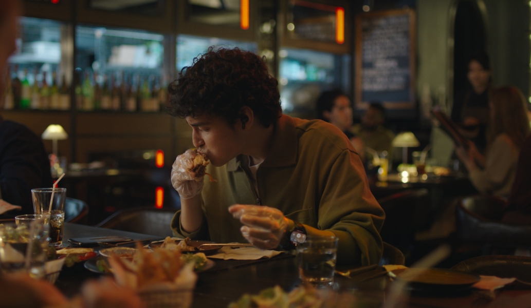 一位佩戴华为擎云 H7556 的男人正在吃披萨，双手不方便触碰手机屏幕，通过手指操控来切换手机视频